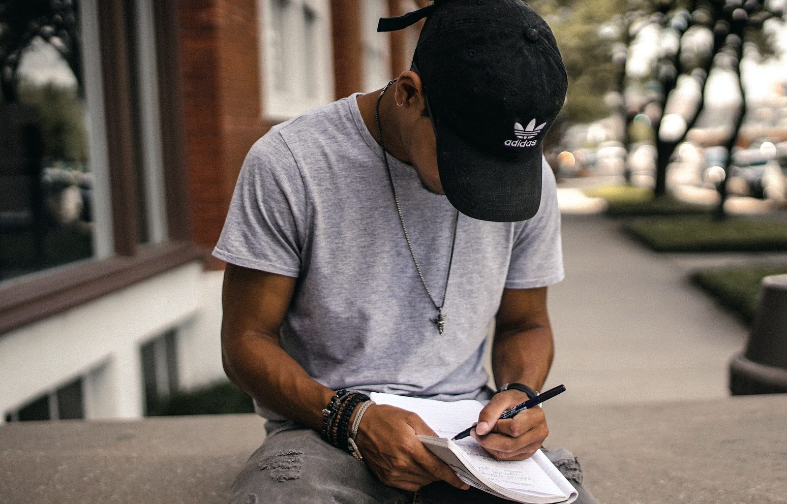 person in black adidas cap sitting on bench writing on notebook