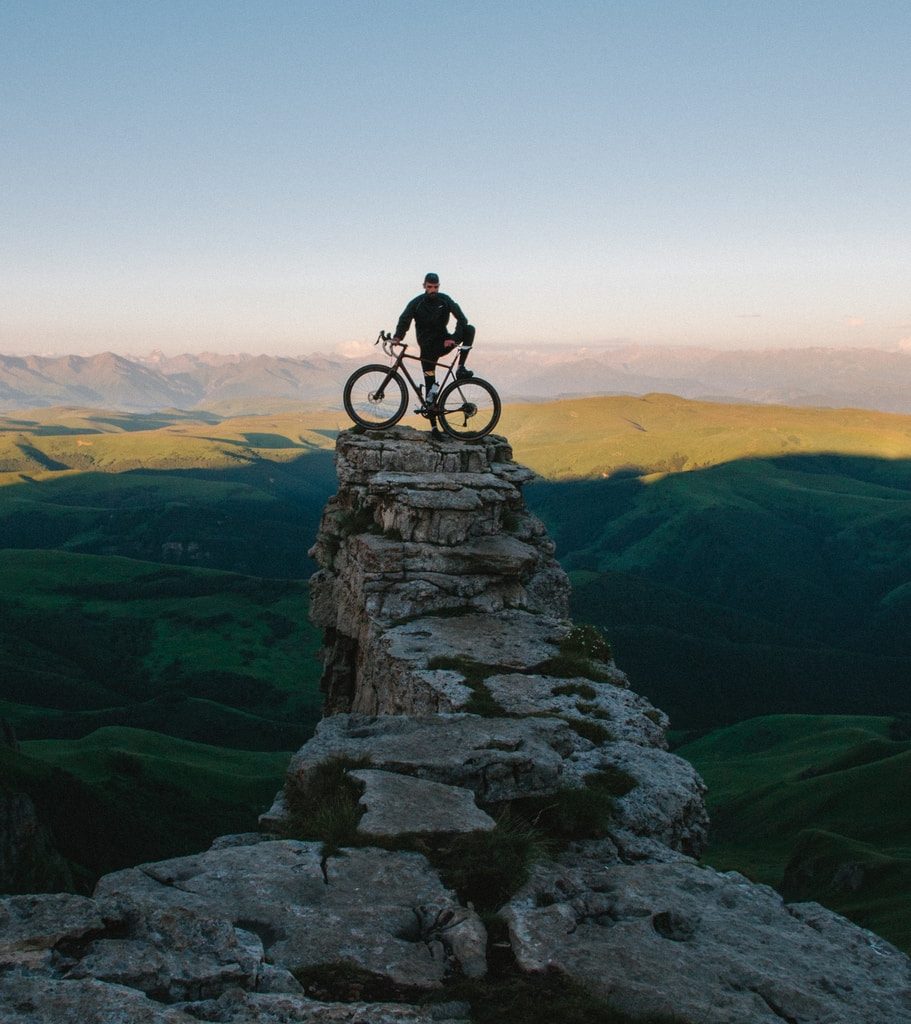 man holding bike while standing on gray mountain