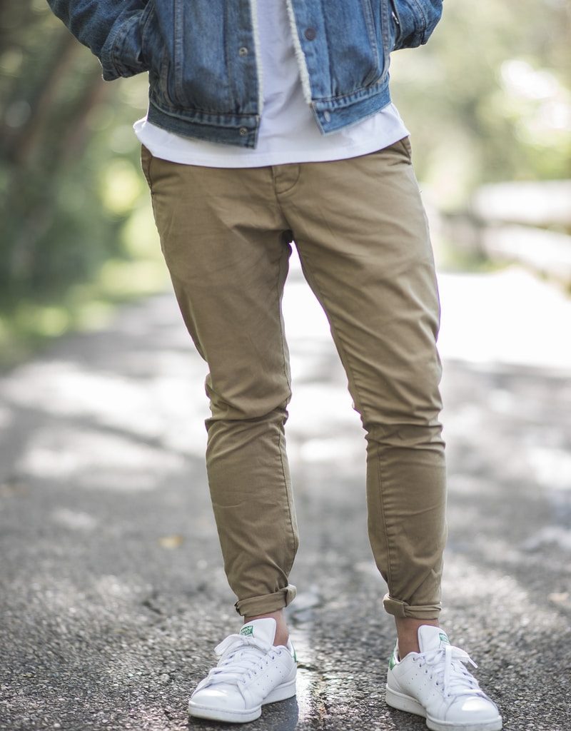 man wearing brown fitted jeans and sneakers standing on road at daytime