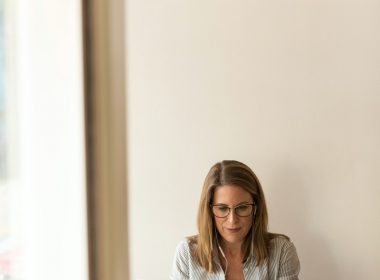 woman wearing grey striped dress shirt sitting down near brown wooden table in front of white laptop computer