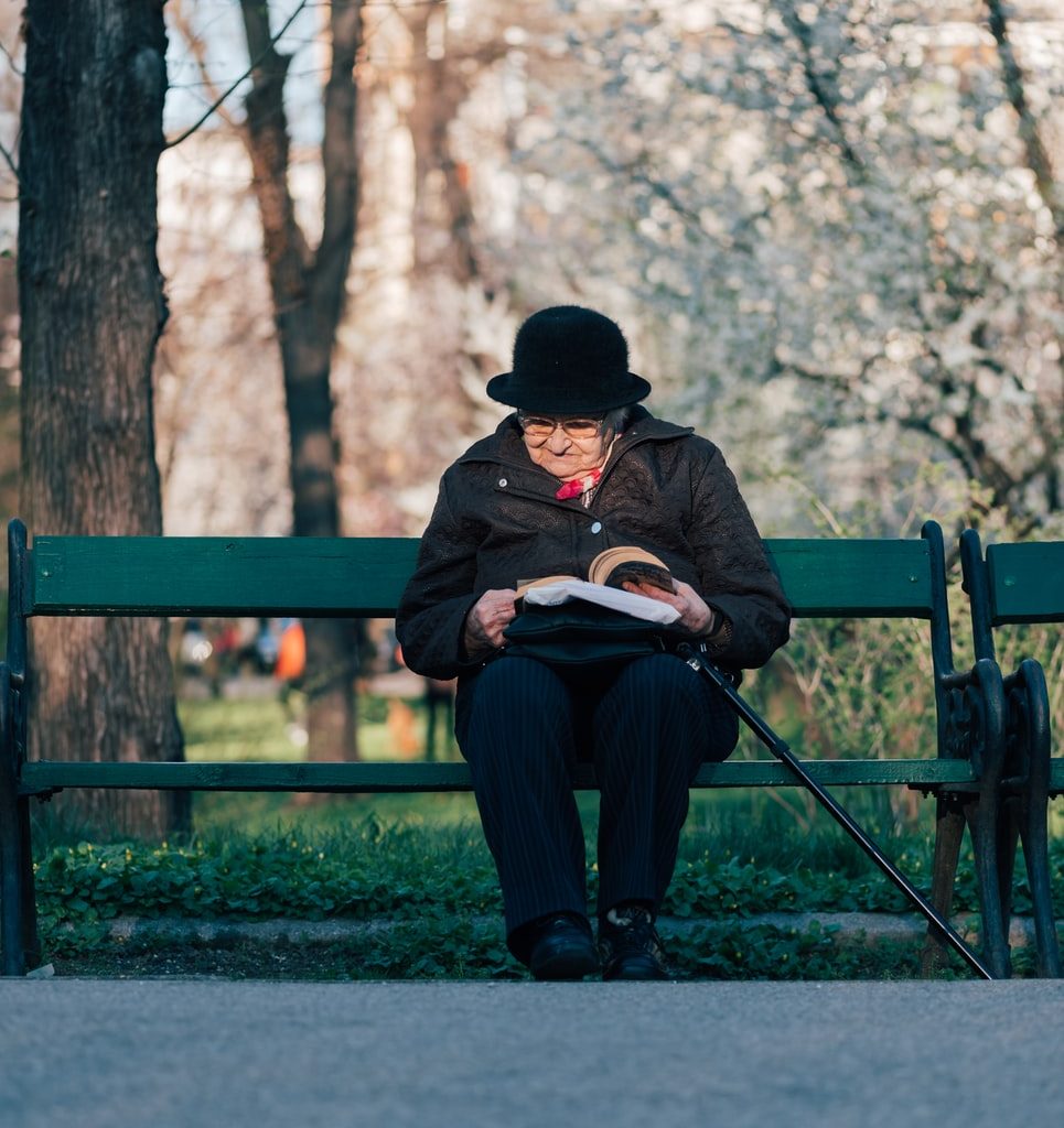 person sits on bench reading book in front of tree at daytime