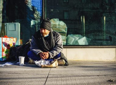man in black and gray jacket sitting on sidewalk during daytime
