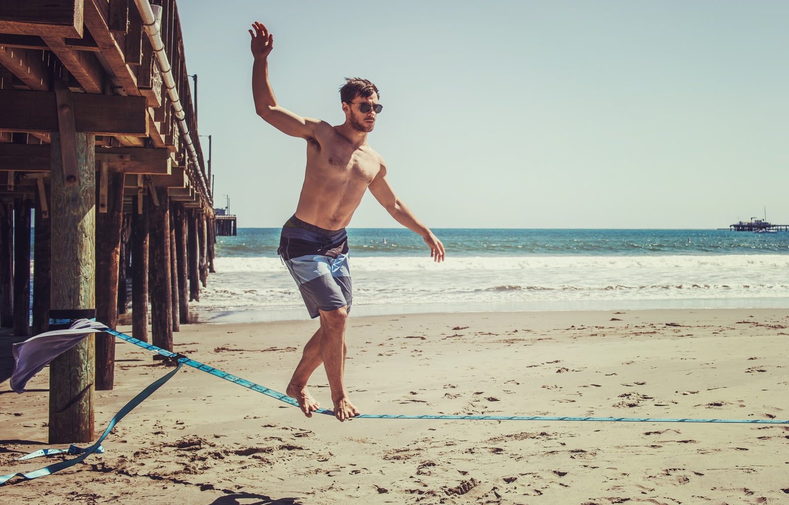 man wearing sunglasses and board shorts standing on rope
