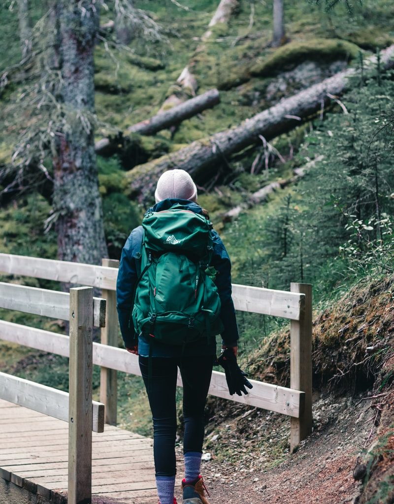 person in green and black jacket and black pants standing on brown wooden bridge during daytime