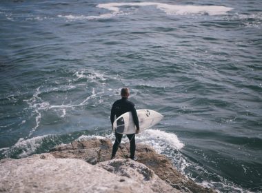 man holding surfboard standing in front of sea