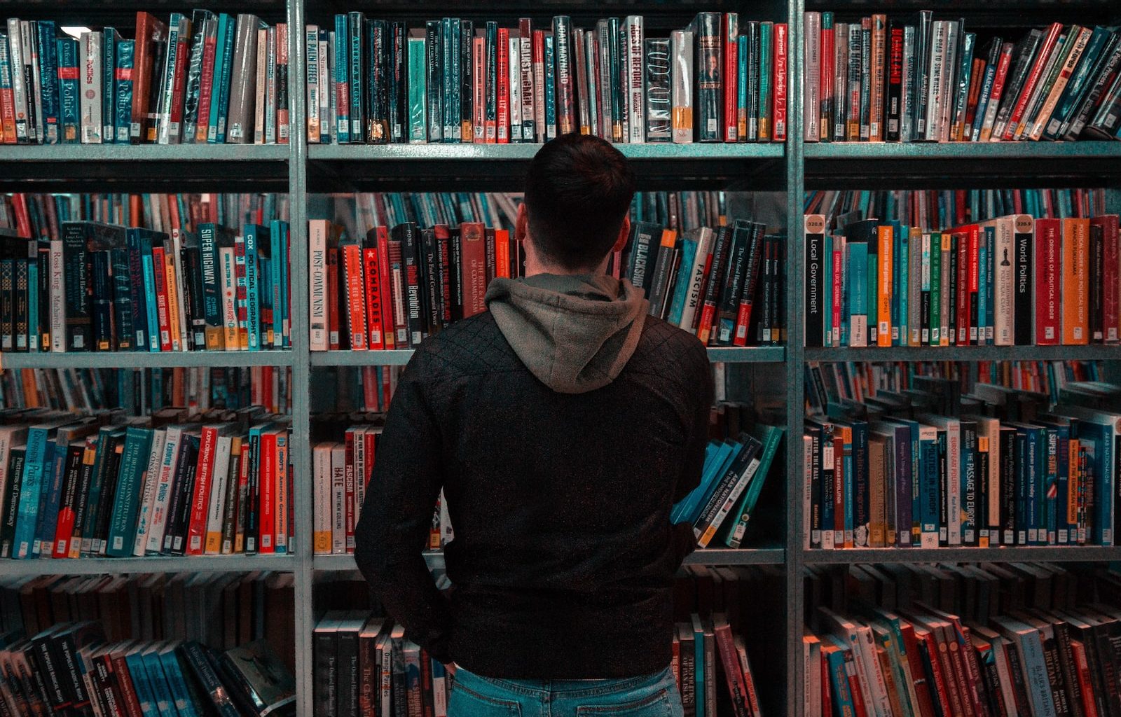 person wearing black and gray jacket in front of bookshelf